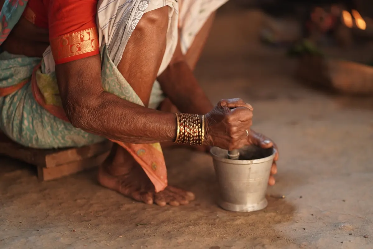 A woman's bangled hands grinding spices at a stone mortar
