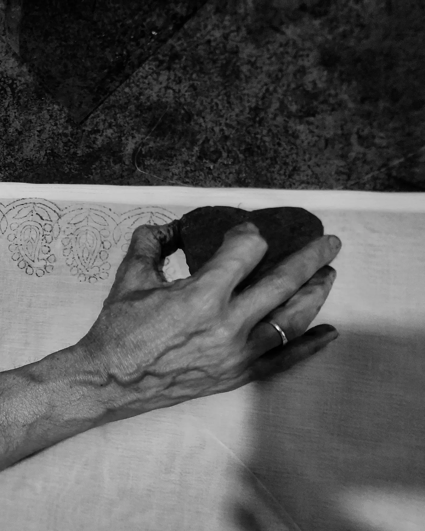 An artisan's hand pressing a carved wooden block onto cloth, mid-print